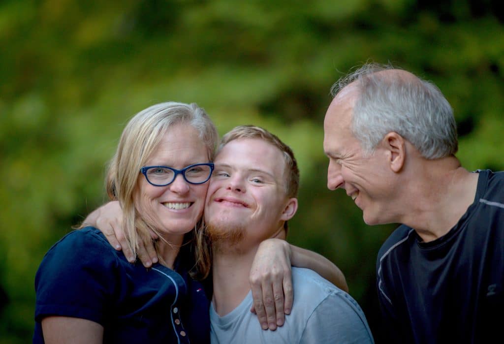 Three people smiling together outdoors with green foliage background, appearing happy and relaxed.