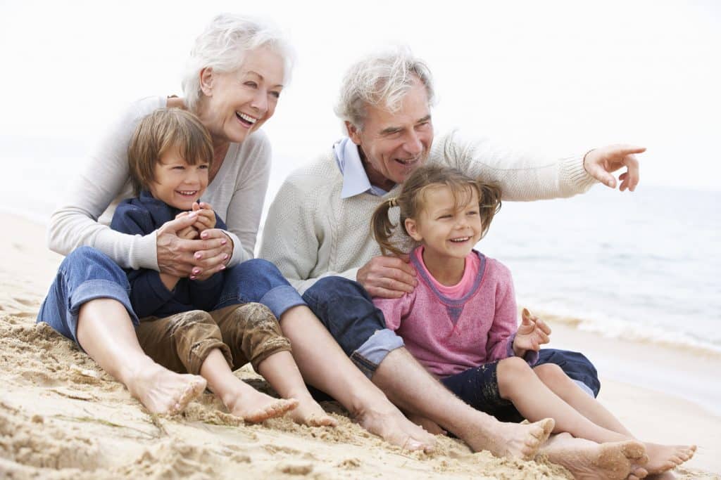 Grandparents and two grandchildren sitting together on sandy beach by ocean.
